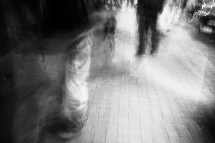 Imagen urbana en blanco y negro en movimiento en donde sólo se ven piernas caminando de personas cortadas por el encuadre. Fotografía por Freddy Briones Parra.